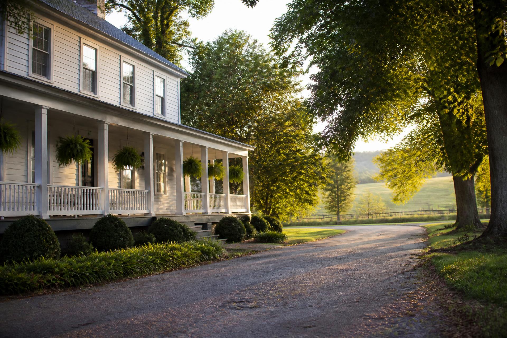 A white farmhouse with a deep front porch on a quiet Tennessee road in evening light